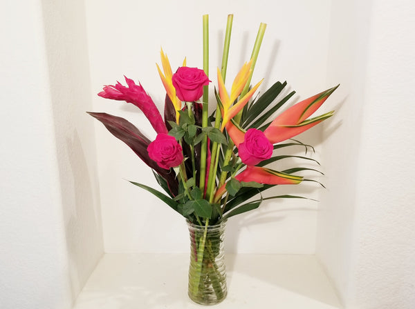 "Who wouldn't love a tropical vacation? This bouquet of red Roses and tropical flowers in a clear glass vase is the next best thing! Tropical Getaway will bring a touch of paradise to any side table or desk. " .