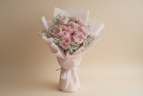 Bouquet of pink roses with baby's breath wrapped in light pink paper on a beige background