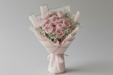 Bouquet of pink O Hara Roses wrapped in pink paper on a white surface with a gray background