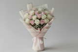 Bouquet of pink and white roses wrapped in white paper with a bow on a light gray background