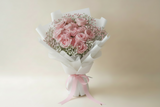 Bouquet of pink roses with baby's breath wrapped in white paper on a light gray background