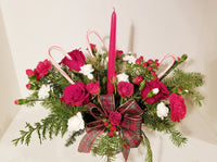 Your loved ones will be feeling merry and bright when they receive this centerpiece of festive holiday spirit. With red roses, red and white carnations, red hypericum berries and Christmas greens, vibrant red blooms make a bold statement with your holiday decor. Set around a tall red tapper candle and natural pinecone pics, there really is no better way to dress up the table than with the Christmas Candle Centerpiece.