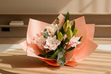 Bouquet of Roselily flowers wrapped in pink paper against a neutral background