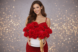 Woman in a red dress holding a large arrangement of red Fancy Carnation flowers against a gray background