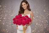 Woman holding a large bouquet of red flowers against a blurred background with bokeh lights.