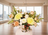 Floral arrangement with yellow, white, and peach flowers in a clear vase on a light background