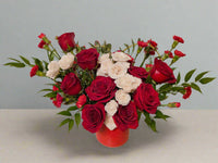 Bouquet of red and white roses in a red vase on a light background