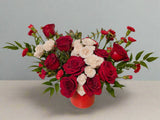 Bouquet of red and white roses in a red vase on a light background