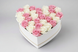 Heart-shaped arrangement of pink and white roses in a white box held by a person.