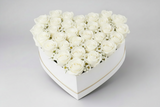Heart-shaped arrangement of white roses in a white box held by a person.