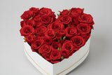 Heart-shaped arrangement of red roses in a white box held by a person.