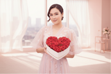Woman holding a heart-shaped box of red roses in a softly lit room.