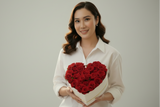 Woman holding a heart-shaped arrangement of red roses against a plain background