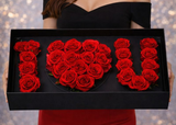 Person holding a black box with red roses shaped like 'I ❤️ U' against a blurred background