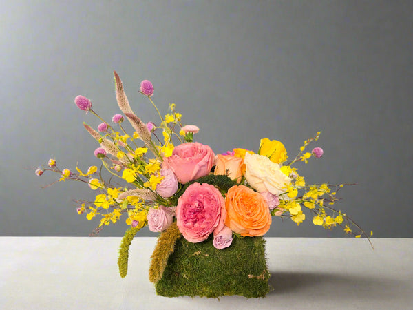 Purse Of Happiness features a mossed “purse” tucked overflowing with the sweetest Roses, seasonal flowers and greenery.