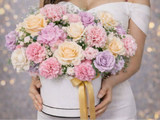 Bouquet of pastel flowers held by a person in a white dress against a blurred background