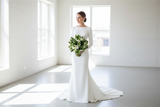Bride in a white wedding dress holding a bouquet of flowers in a bright room.