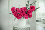 Pink flowers in a white vase on a small round table with a blurred indoor background