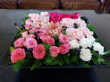 Modern grouping arrangement in a black or white square tray (size: 13” x 13” x 3”), mainly using roses, carnations, Chrysanthemum, berries and greenery. 