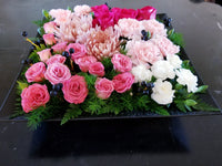 Modern grouping arrangement in a black or white square tray (size: 13” x 13” x 3”), mainly using roses, carnations, Chrysanthemum, berries and greenery. 