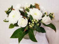 glorious arrangement evokes the splendor of winter in a forest. white Roses, Carnations, Holly Berries, Chrysanthemums, Poms, and magnolia tips